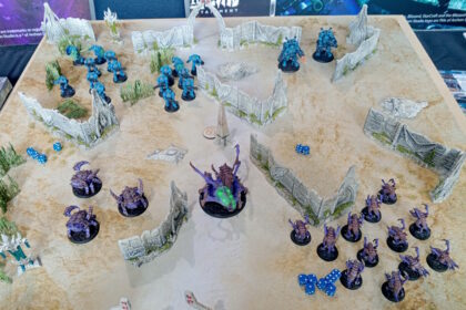 StarCraft TMG - laufende Partie Protoss gegen Zerg auf dem Demotisch mit Terrain und Wuerfeln (Quelle: https://www.tabletopbattles.com/first-look-the-starcraft-tabletop-miniatures-game)