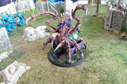 StarCraft TMG - bemalte Zerg-Queen auf dem Spieltisch, im Hintergrund Terran-Marines und Ruinengelaende (Quelle: https://www.tabletopbattles.com/starcraft-tmg-swarmlings-the-new-meta-gho-2026-starcraft-battle-report)