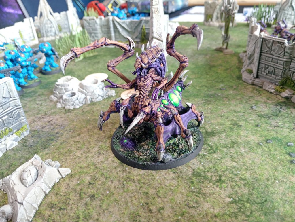 StarCraft TMG - bemalte Zerg-Queen auf dem Spieltisch, im Hintergrund Terran-Marines und Ruinengelaende (Quelle: https://www.tabletopbattles.com/starcraft-tmg-swarmlings-the-new-meta-gho-2026-starcraft-battle-report)